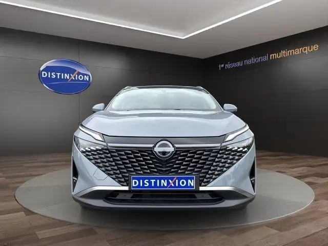 Vue frontale du Nissan Qashqai gris foncé 2025 avec calandre noire géométrique et logo central lumineux.