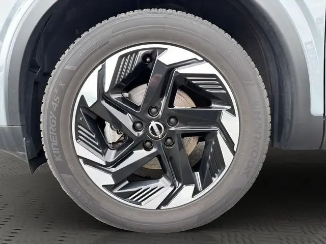 Gros plan sur la roue avant droite du Nissan Qashqai gris foncé, avec jante alliage noire et argentée au design moderne.