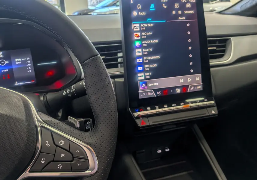 Intérieur du Renault Captur 2025 Mild Hybrid, vue sur le volant perforé et l'écran tactile central affichant la radio.