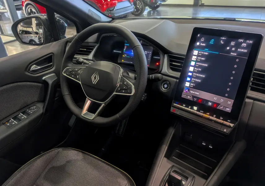 Vue intérieure du tableau de bord du Renault Captur 2025 gris rafale, avec volant multifonction et écran tactile vertical.