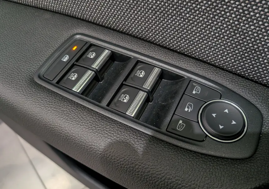 Gros plan sur les commandes de lève-vitres et rétroviseurs électriques sur la porte intérieure tissu gris du Renault Captur 2025.