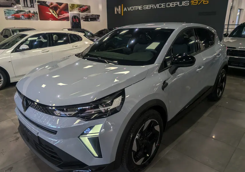 Vue 3/4 avant droite du Renault Captur gris rafale 2025 avec feux LED et jantes noires bicolores en showroom.