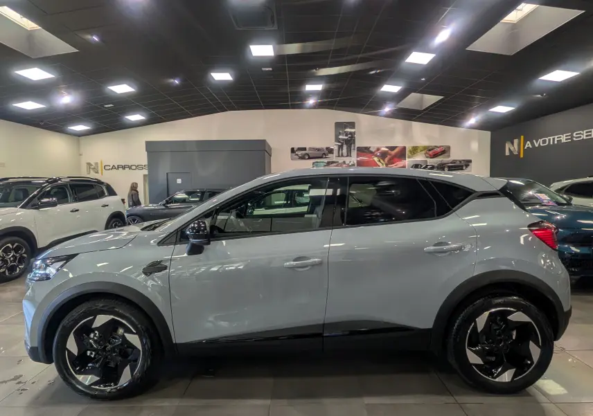 Profil côté gauche du Renault Captur gris rafale 2025 avec jantes biton noires et toit noir en showroom.