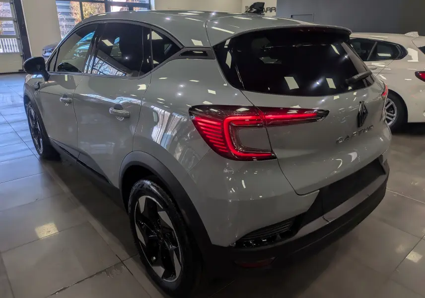 Vue 3/4 arrière droite du Renault Captur 2025 gris rafale avec feux arrière LED et jantes bi-ton en showroom.
