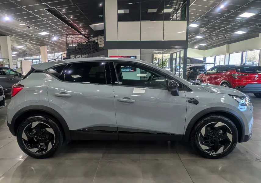 Profil côté droit du Renault Captur 2025 gris rafale avec jantes biton et toit noir en showroom.