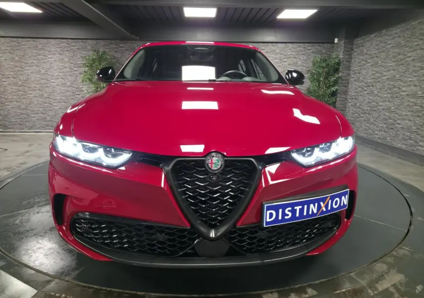 Vue frontale d'une Alfa Romeo Tonale rouge avec calandre noire et phares LED allumés dans un showroom.