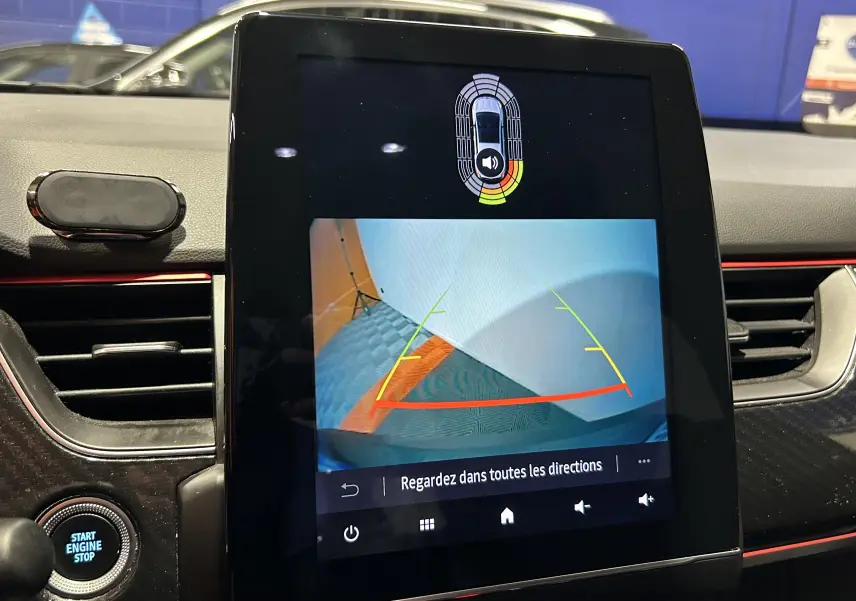 Écran central tactile montrant la caméra de recul avec alertes de proximité sur Renault Arkana noir, vue intérieure avant.