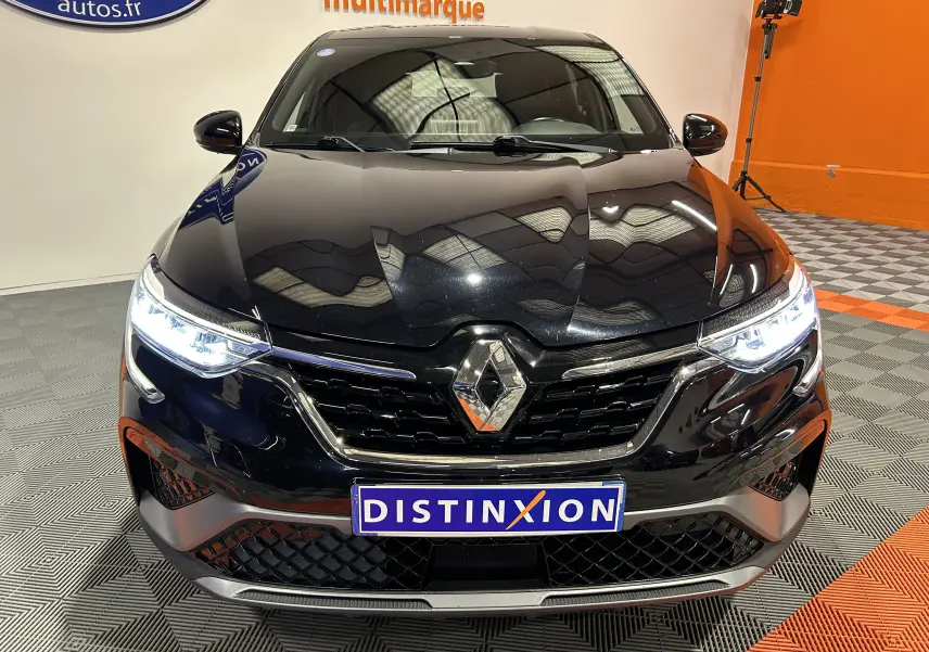 Vue avant rapprochée d’un Renault Arkana noir avec phares allumés et calandre chromée dans un showroom.