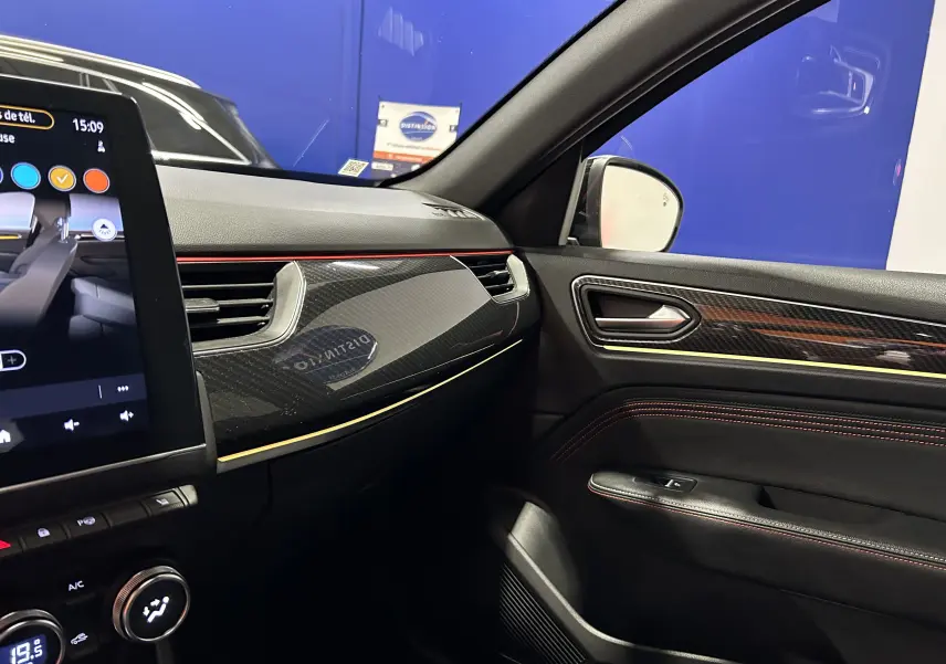 Intérieur côté passager du Renault Arkana noir, tableau de bord et porte avec inserts carbone et surpiqûres rouges.