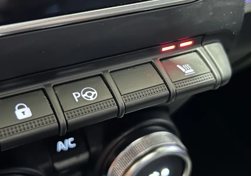 Gros plan sur les boutons de commande du tableau de bord du Renault Arkana noir, avec témoin de siège chauffant allumé.