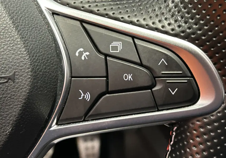 Gros plan sur les commandes multifonctions noires du volant perforé de la Renault Arkana E-Tech noire.