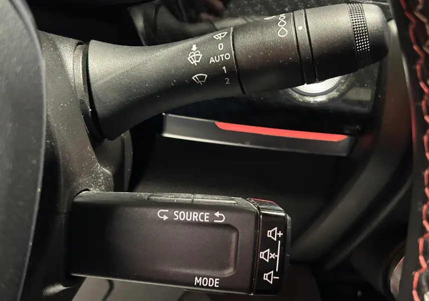 Gros plan sur les commandes au volant noir du Renault Arkana E-Tech, avec boutons source et mode visibles.