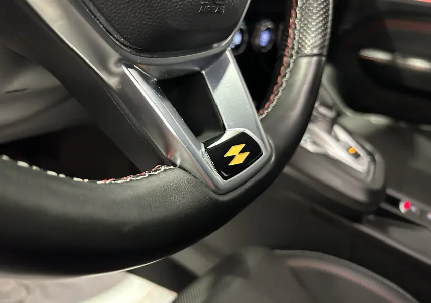 Gros plan sur le volant noir avec surpiqûres rouges et logo jaune, intérieur du Renault Arkana E-Tech 2022.