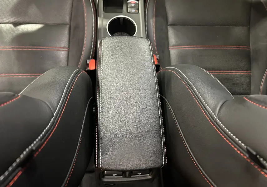 Vue plongeante sur l'accoudoir central noir avec surpiqûres rouges entre les sièges avant en cuir noir du Renault Arkana E-Tech.