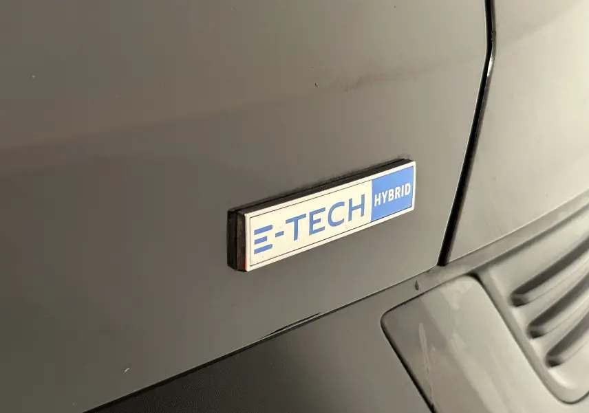 Gros plan sur l'écusson E-Tech Hybrid bleu et blanc sur la carrosserie noire d'un Renault Arkana.