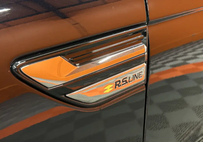 Gros plan sur l'emblème RS Line chromé sur la portière noire d'une Renault Arkana hybride.