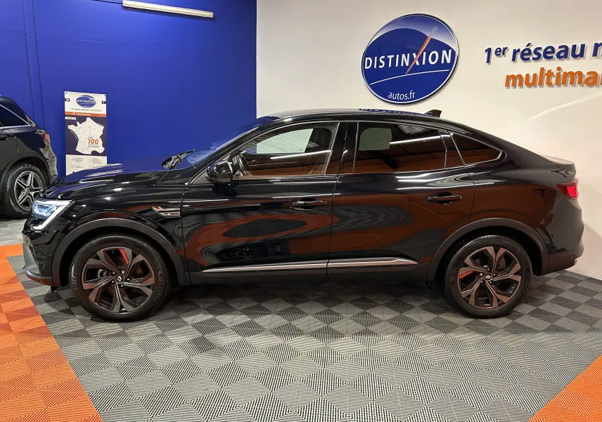 Vue de profil côté gauche d'une Renault Arkana E-Tech noire avec jantes noires et détails RS Line en intérieur showroom.
