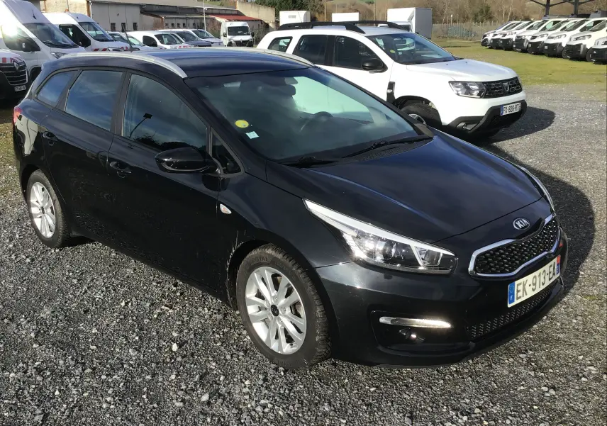 KIA CEE'D SW noire vue en 3/4 avant droit sur un parking, avec jantes alliage et feux allumés.