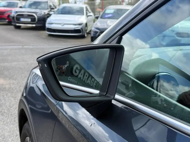 Rétroviseur côté gauche d’un SEAT Arona 2025 gris Magnétique Métal avec affichage d’angle mort, vue rapprochée extérieure.