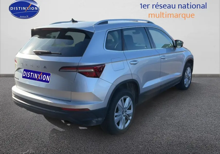 Vue 3/4 arrière droite d'un Skoda Karoq gris avec barres de toit et feux arrière LED sur fond neutre.