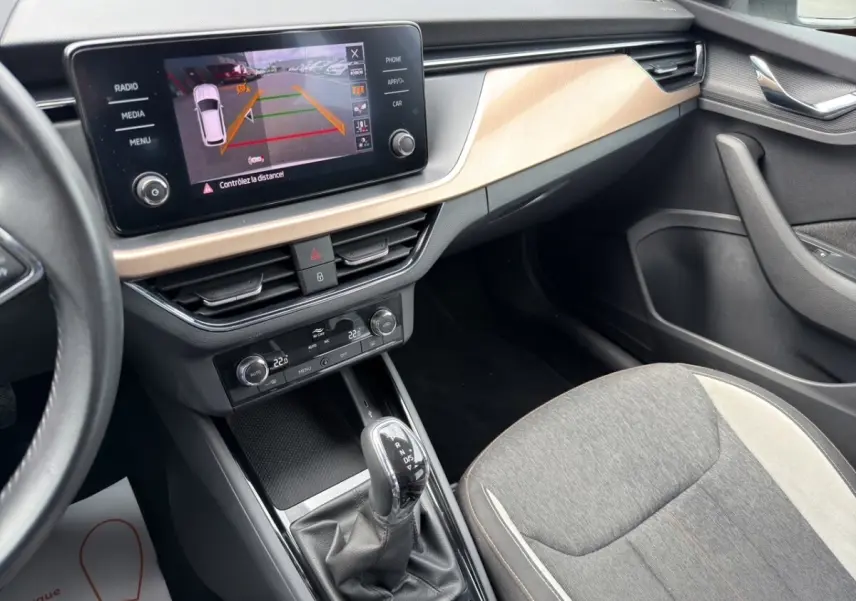 Vue intérieure côté passager du Skoda Kamiq 2023, écran tactile avec caméra de recul et sellerie tissu gris clair.
