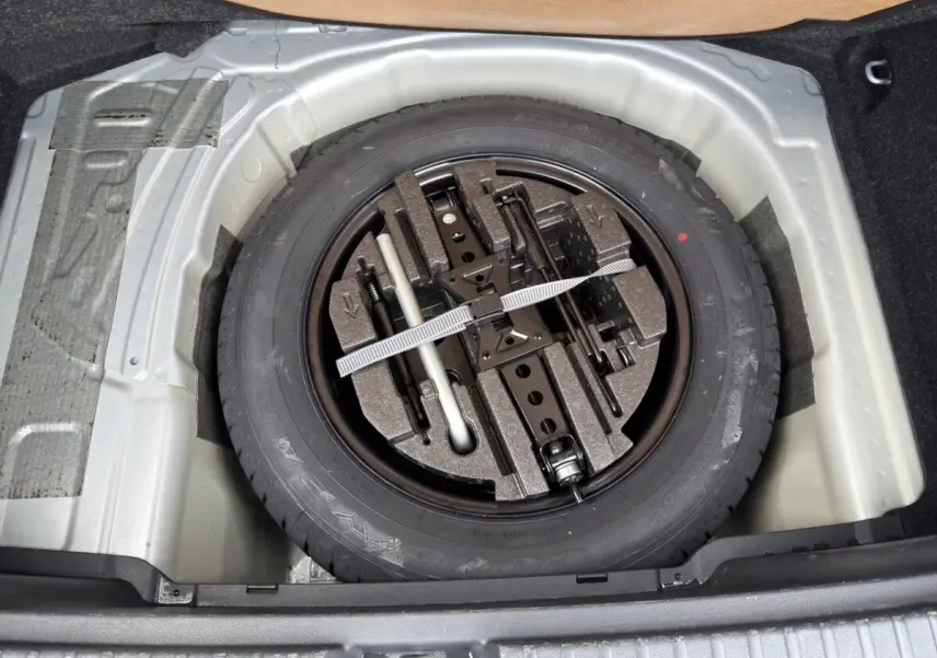 Gros plan sur la roue de secours galette noire et ses outils, logée dans le coffre du Skoda Kamiq gris clair 2023.