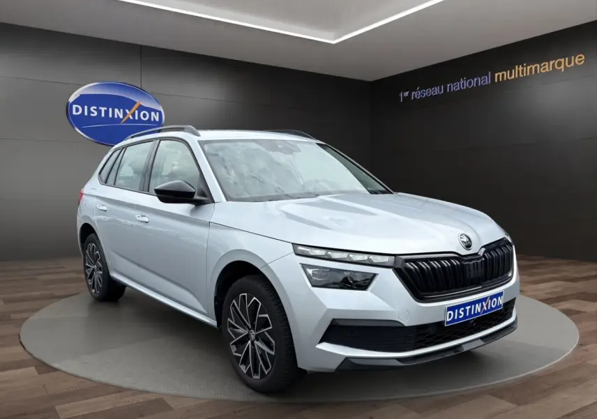 Skoda Kamiq gris clair en 3/4 avant droit, avec jantes bi-ton et rétroviseurs noirs rabattables.