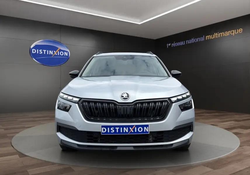 Vue avant d'un Skoda Kamiq gris clair avec calandre noire et feux LED, présenté en showroom Distinxion.