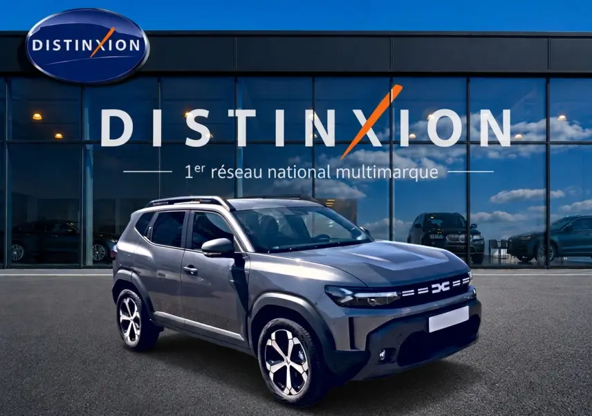 Vue 3/4 avant droit du Dacia Duster gris schiste 2026 avec jantes alu et barres de toit devant un showroom Distinxion.