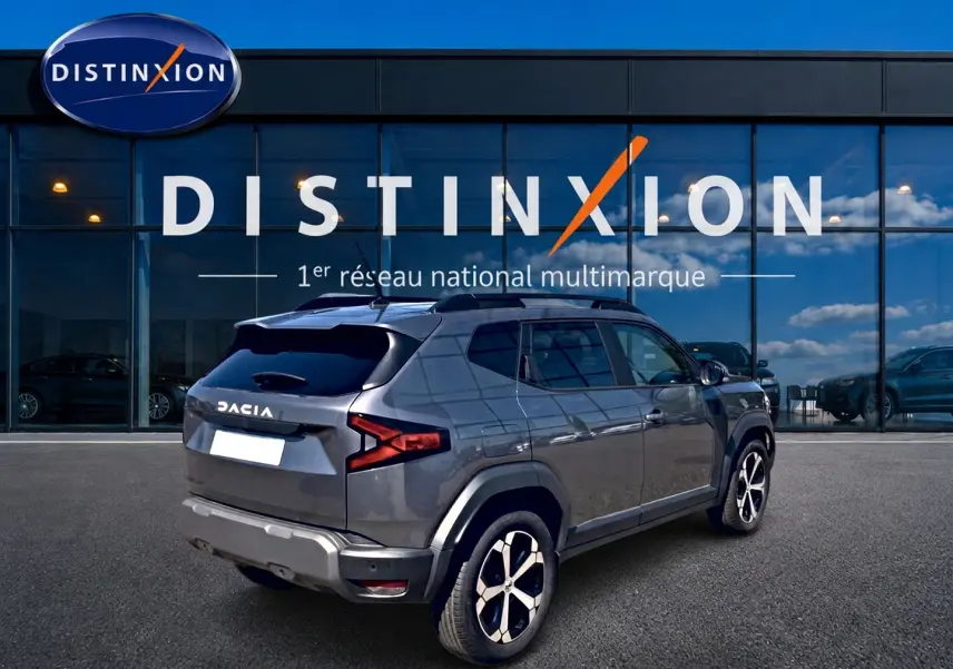 Vue 3/4 arrière droite d'un Dacia Duster gris schiste avec jantes alu, garé devant une vitrine Distinxion.