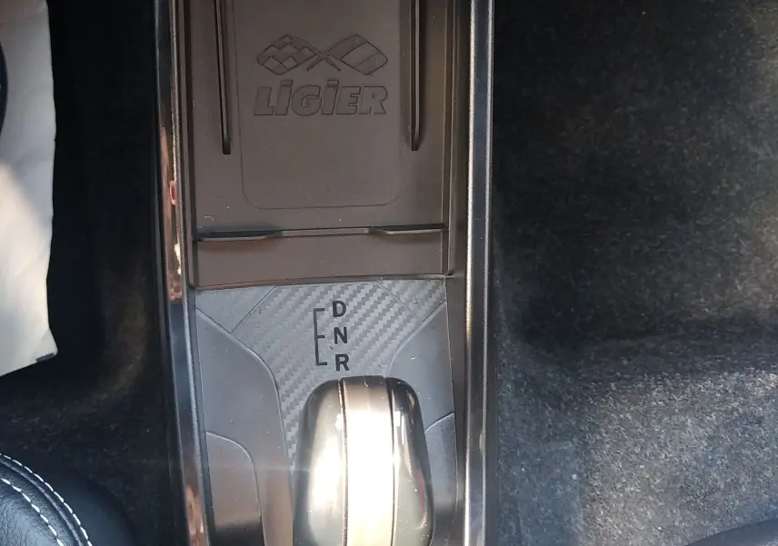 Vue plongeante sur la console centrale noire avec levier de boîte auto et logo Ligier en finition carbone.