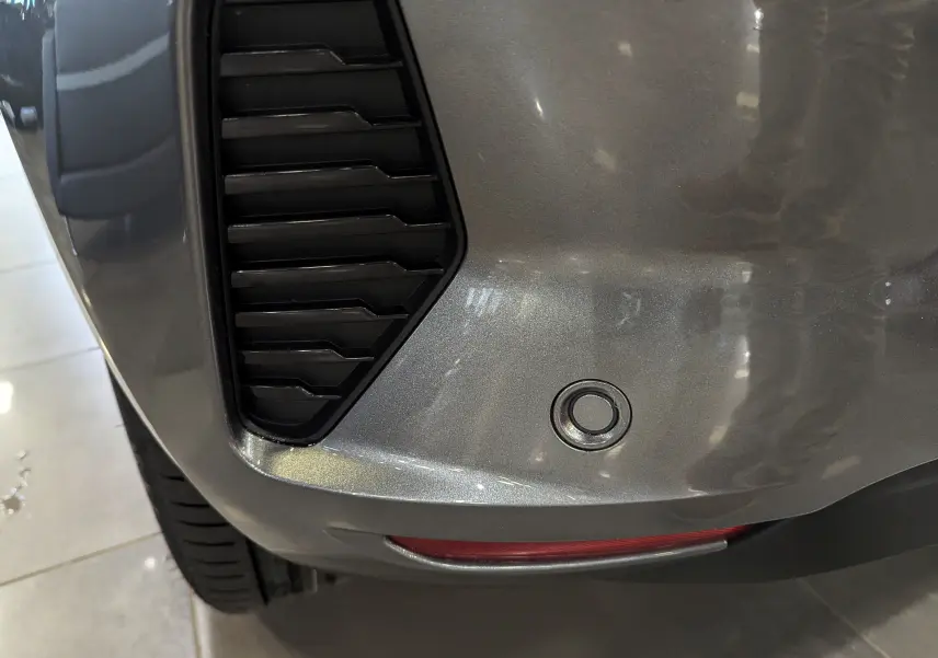 Gros plan sur le pare-chocs arrière gris schiste d'une Renault Clio V, avec capteur de recul et partie de l'aération noire.