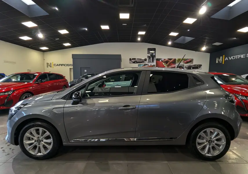 Profil côté gauche d'une Renault Clio V Blue dCi 100 CH Evolution gris schiste dans un showroom lumineux.