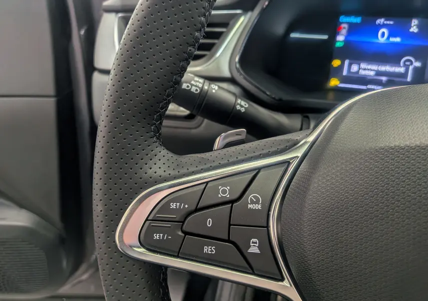 Gros plan sur les commandes au volant en cuir perforé du Renault Captur 2025, affichage digital bleu en arrière-plan.