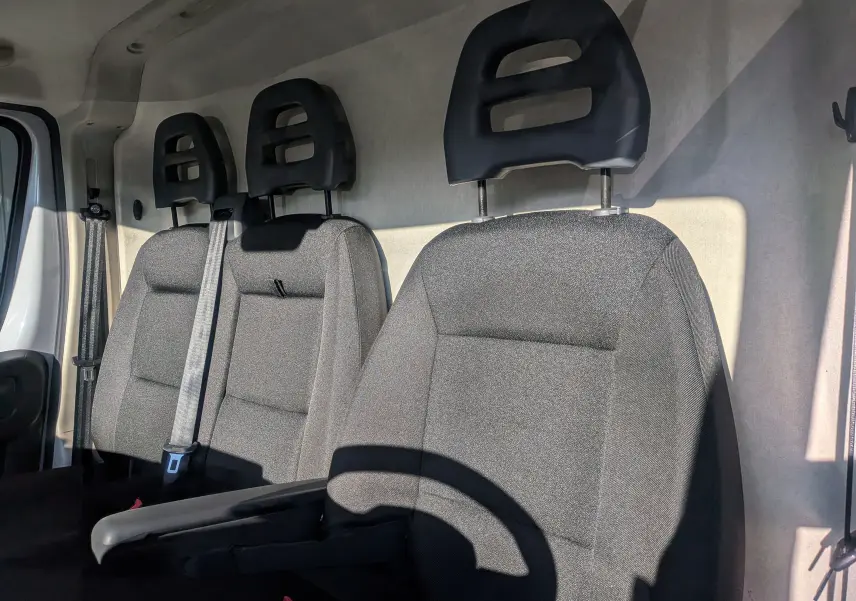 Intérieur du FIAT Ducato Fourgon blanc 2022, vue latérale des sièges avant en tissu gris avec appuie-têtes noirs.