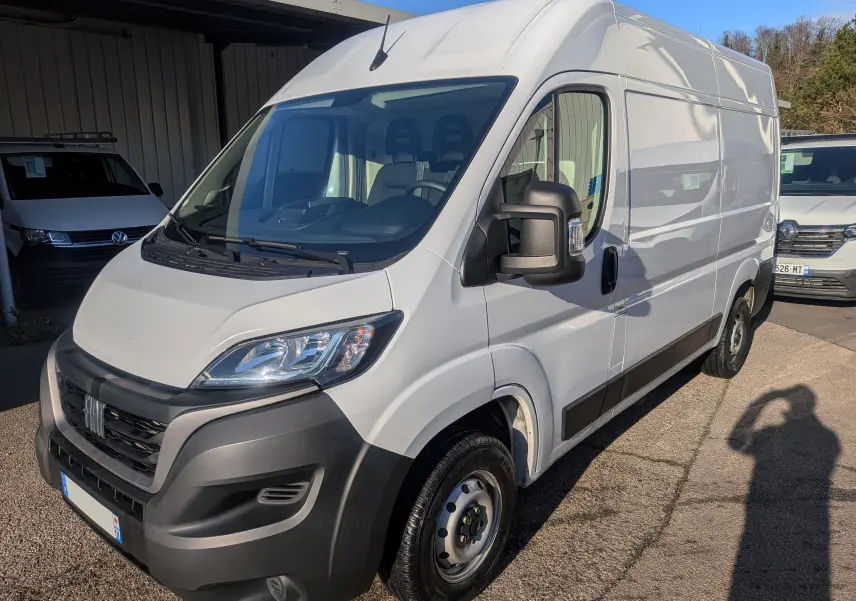 Vue 3/4 avant droite d’un FIAT Ducato Fourgon blanc 2022 avec pare-chocs noir et rétroviseurs larges, stationné en extérieur.