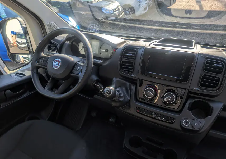 Vue intérieure du poste de conduite du Fiat Ducato Fourgon blanc 2022, avec volant, tableau de bord et levier de vitesses manuel.