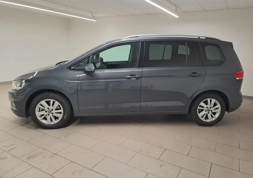 Vue de profil côté gauche d'un Volkswagen Touran gris dauphin 2024 dans un intérieur neutre, sans attelage visible.