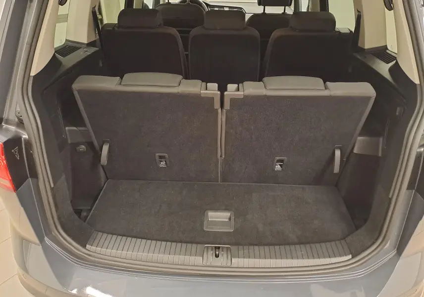 Vue arrière du coffre ouvert d'un Volkswagen Touran gris Dauphin 2024 avec sièges arrière relevés et espace de chargement visible.