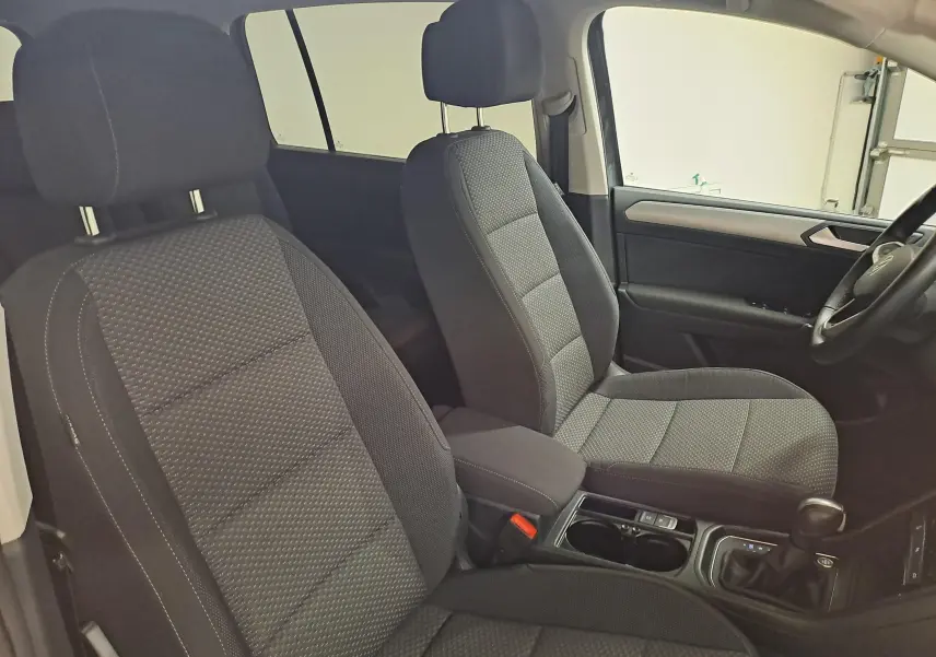 Vue intérieure côté avant droit du Volkswagen Touran 2024, sièges tissu gris avec console centrale et levier de boîte automatique.