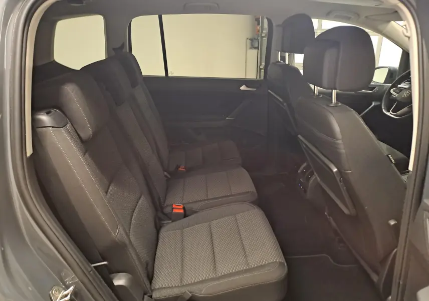 Vue intérieure côté gauche du Volkswagen Touran 2024, montrant la banquette arrière en tissu gris et les sièges avant.