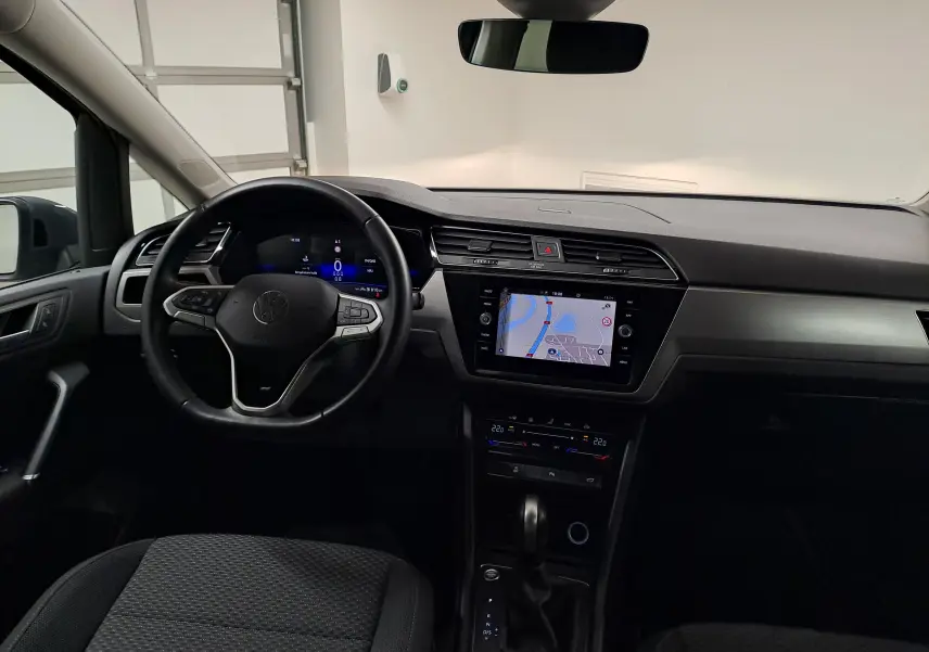 Vue intérieure avant du Volkswagen Touran 2024, tableau de bord noir avec écran tactile et volant multifonction.