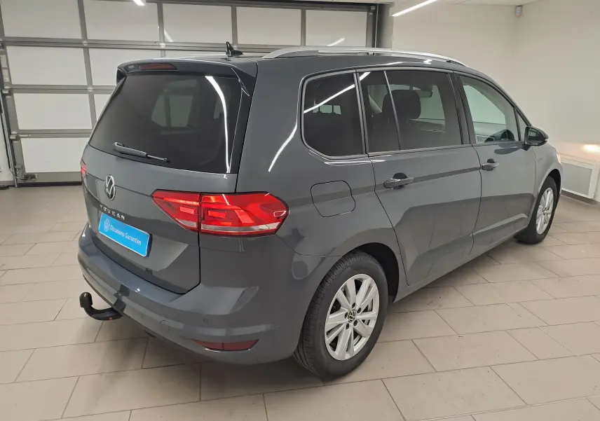 Vue 3/4 arrière droite d'un Volkswagen Touran gris dauphin avec attelage démontable en intérieur showroom.