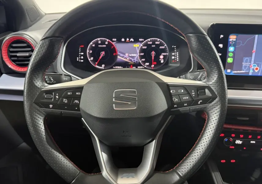 Vue rapprochée du volant cuir perforé noir avec surpiqûres rouges et tableau de bord digital de la SEAT Ibiza 2024 gris foncé.