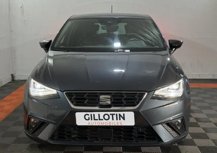 Vue frontale d'une SEAT Ibiza 1.0 TSI 110 FR gris foncé avec phares LED allumés en intérieur.