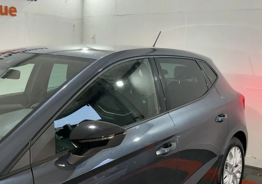 Vue côté gauche arrière d'une SEAT Ibiza gris foncé 2024 avec rétroviseur noir et jantes argentées.