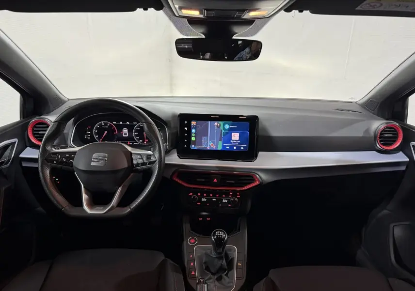 Vue intérieure avant de la SEAT IBIZA 1.0 TSI 110 FR 2024, tableau de bord noir avec touches rouges et écran tactile central.