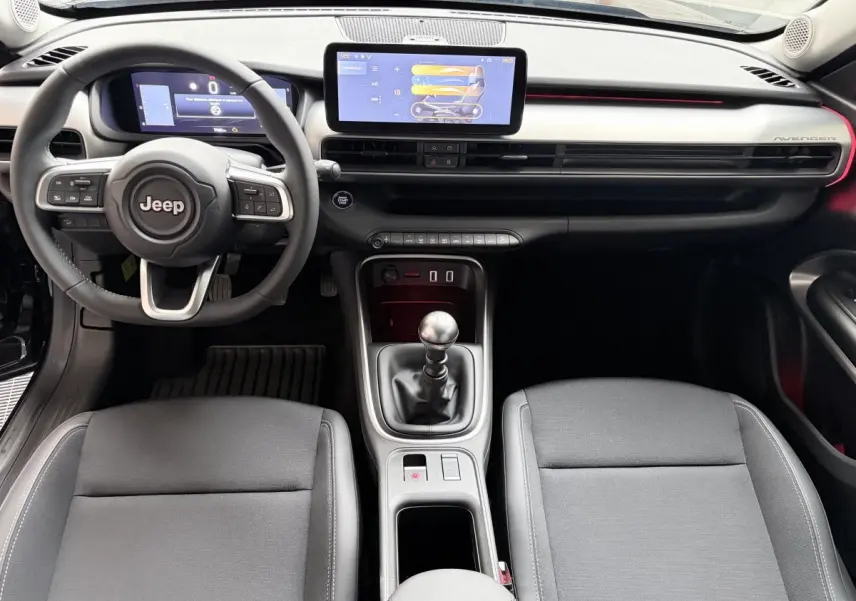 Intérieur Jeep Avenger 2025 vu de face, volant cuir, écran tactile central 10,25 pouces et levier de vitesse manuel.