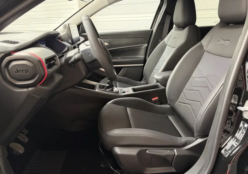 Vue intérieure côté conducteur du Jeep Avenger 2025 noir, sièges tissu avec logo Jeep brodé et volant multifonctions.