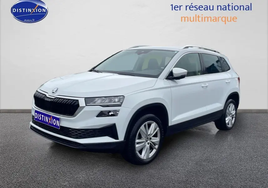Vue 3/4 avant droite d’un Skoda Karoq blanc glacial avec jantes alu et barres de toit visibles.